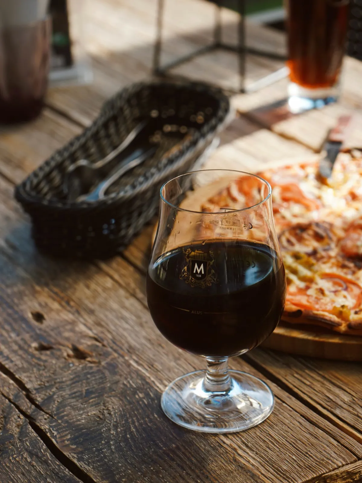 Pica uz koka dēļa un glāze tumšā alus uz terases galda